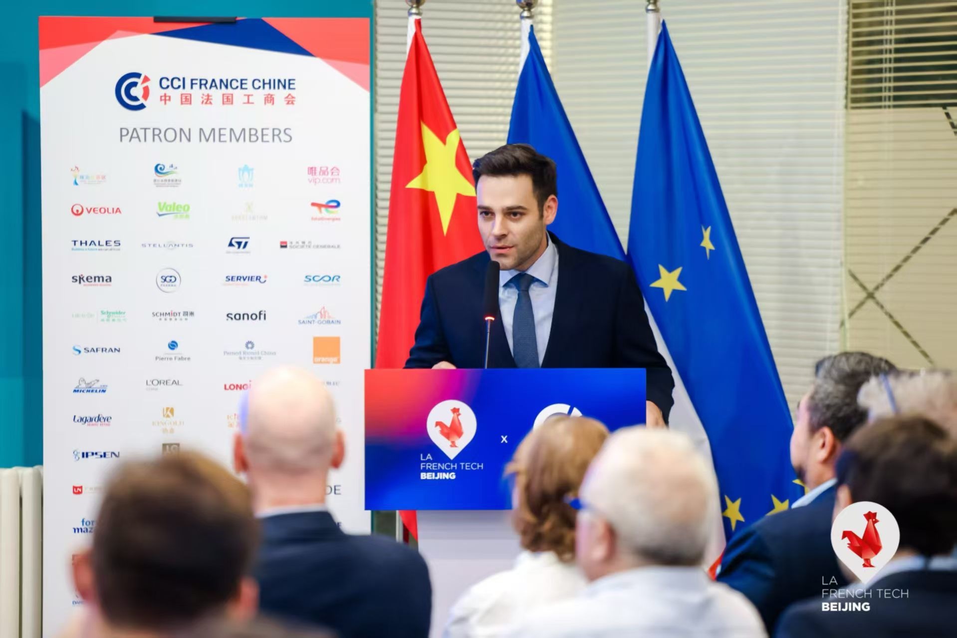 Le président de la French Tech Beijing au pupitre devant le panneau des membres de la CCI et les drapeaux français, chinois et européen